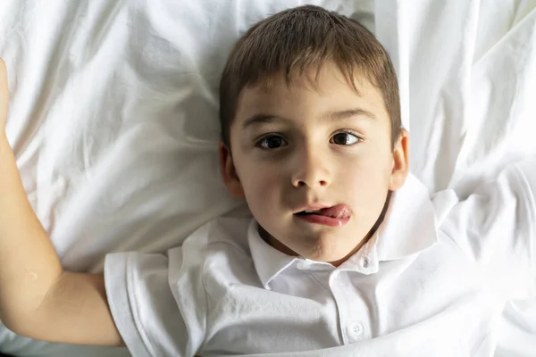 Een kleine jongen lag op het bed met witte deken — Stockfoto