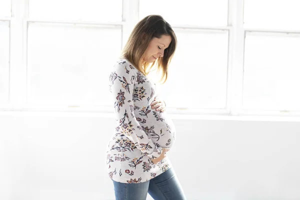 Joven mujer embarazada hermosa de pie cerca de la ventana en casa —  Fotos de Stock