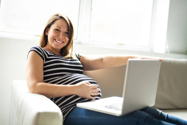 Un ritratto di una bella donna incinta che utilizza il computer portatile giaceva sul divano — Foto Stock