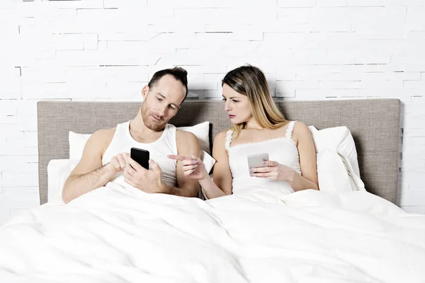 Couple utilisant leur téléphone portable au lit — Photo