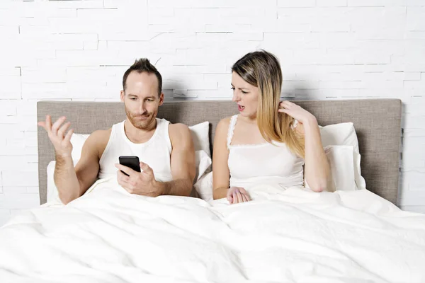 Pár pomocí svého mobilního telefonu v posteli — Stock fotografie