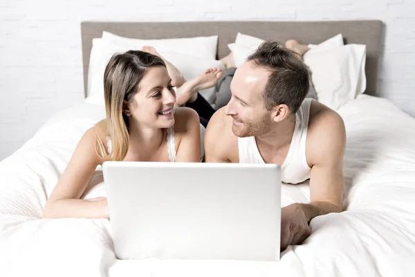 Jolie femme avec mari au lit alors qu'il utilise un ordinateur portable — Photo