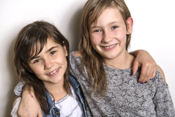 Duas crianças felizes irmã de pé na parede cinza em branco e abraçando — Fotografia de Stock