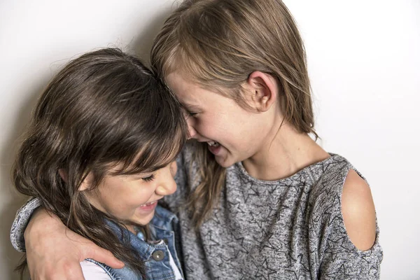 Twee gelukkige jonge geitjes zuster permanent tijdens lege grijze muur en omarmen — Stockfoto