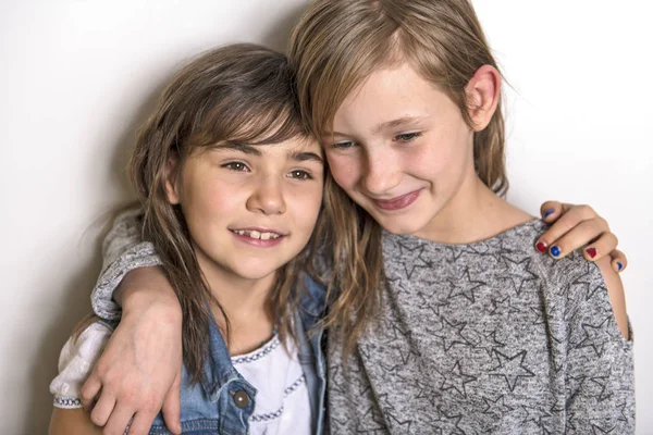 Twee gelukkige jonge geitjes zuster permanent tijdens lege grijze muur en omarmen — Stockfoto