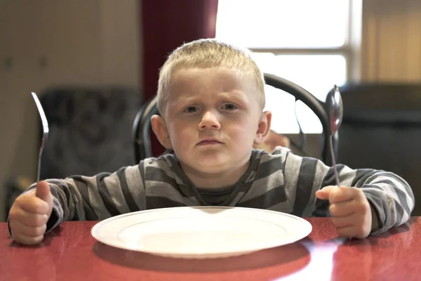 A Upset little boy waiting for dinner while holding a fork and a spoon — Stock Photo, Image
