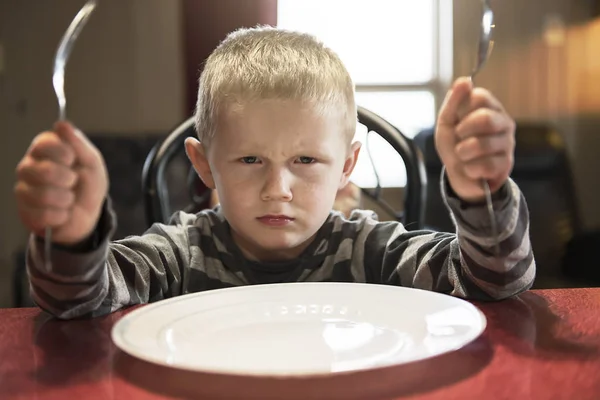A Upset little boy waiting for dinner while holding a fork and a spoon — Stock Photo, Image