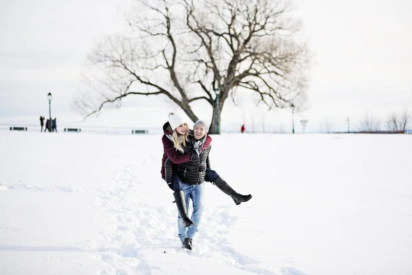 Um jovem casal lá fora no inverno com árvore na parte de trás — Fotografia de Stock