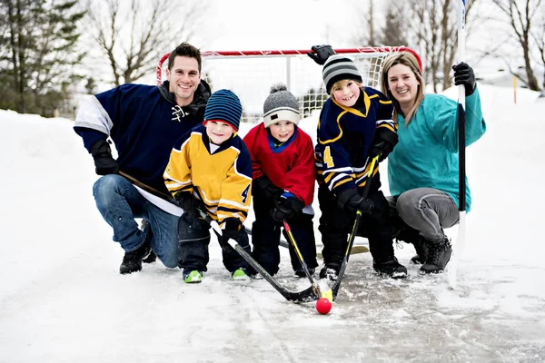 Веселые веселые дети играют в хоккей с отцом и матерью на улице в зимний сезон — стоковое фото