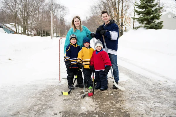 Fröhliche lustige Kinder, die im Winter mit Vater und Mutter auf der Straße Hockey spielen — Stockfoto