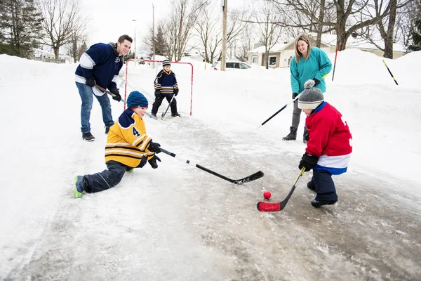 Fröhliche lustige Kinder, die im Winter mit Vater und Mutter auf der Straße Hockey spielen — Stockfoto