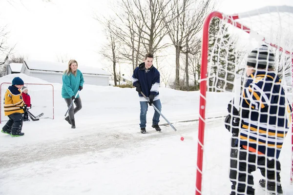 Feliz engraçado crianças jogando hóquei com pai e mãe na rua na temporada de inverno — Fotografia de Stock