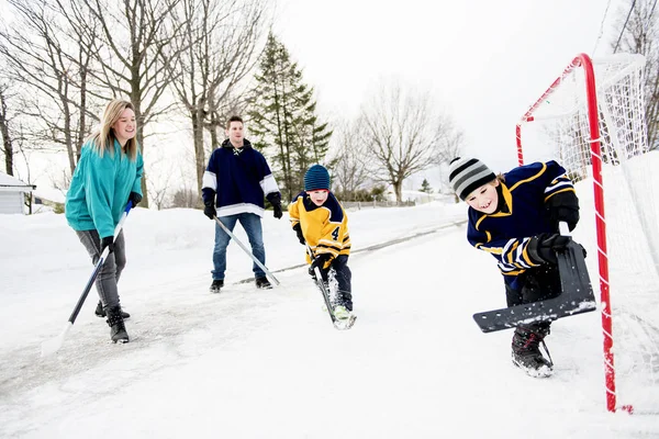 Happy funny kids playing hockey with father and mother on street in the winter season