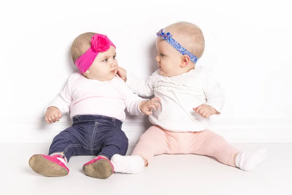 Bebês meninas sentadas no chão sobre a parede branca — Fotografia de Stock