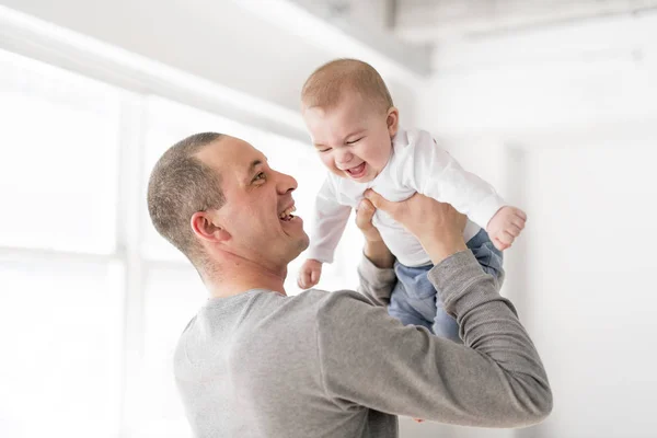 Padre sostiene al bebé en una hermosa habitación con ventanas blancas — Foto de Stock