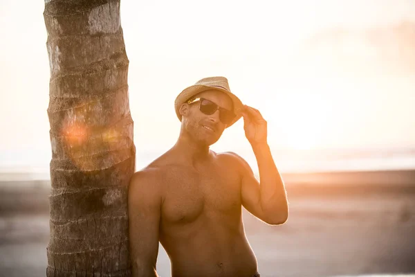 Homme avec chapeau de paille sur la plage au coucher du soleil regarde et sourit et sourit — Photo