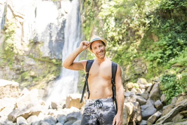 Homme attrayant debout près des cascades sur son dos — Photo