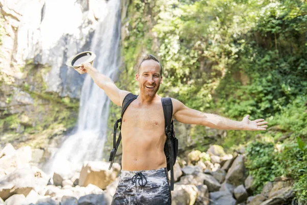 Homme attrayant debout près des cascades sur son dos — Photo