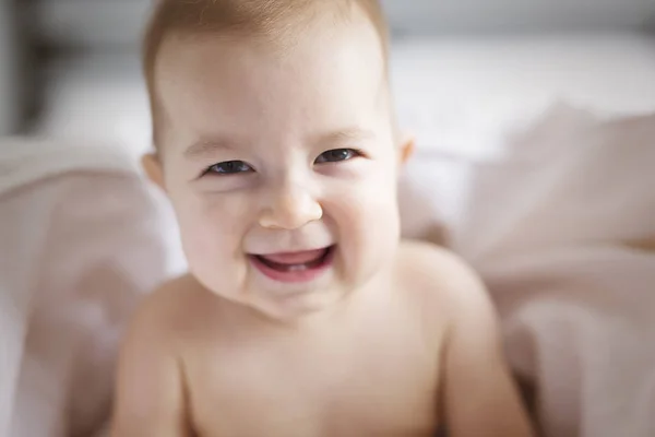 Una bambina siede su un lenzuolo bianco in camera da letto — Foto Stock