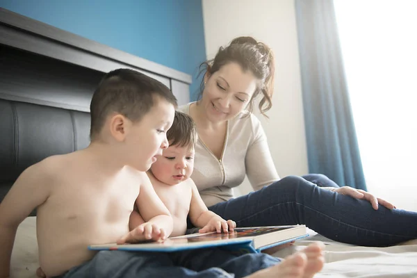 Мама читает книгу с двумя детьми, мальчиками в спальне — стоковое фото