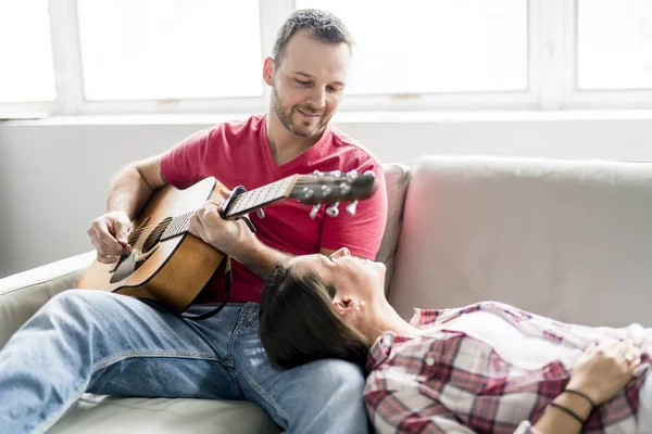Jong (echt) paar zittend op een bank in de woonkamer en gitaar spelen — Stockfoto