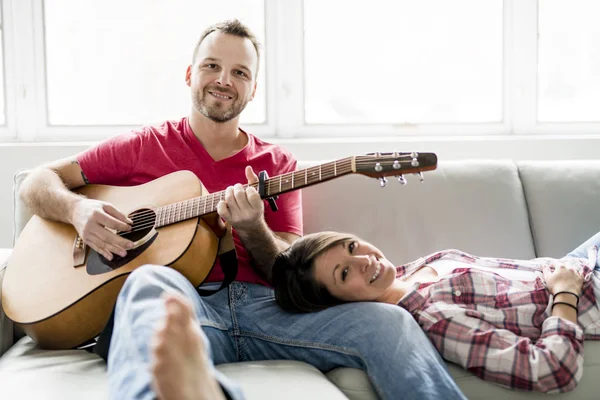 Jong (echt) paar zittend op een bank in de woonkamer en gitaar spelen — Stockfoto