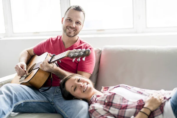 Jong (echt) paar zittend op een bank in de woonkamer en gitaar spelen — Stockfoto