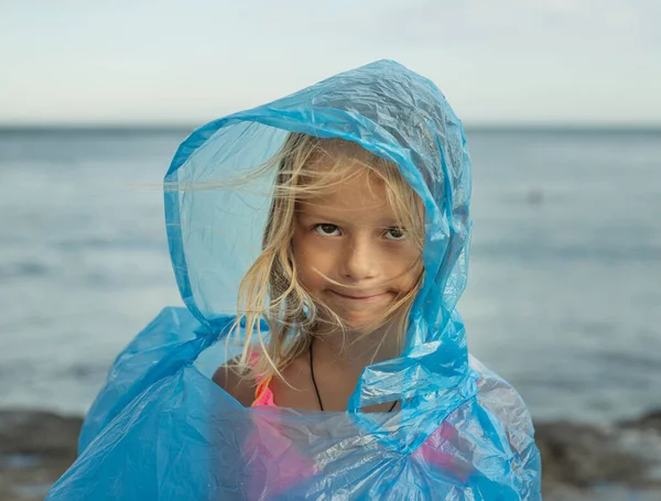 Little girl in plastic transparent raincoat on a windy day at the beach, moody day at the beach