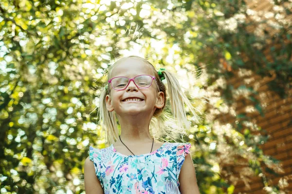 Pequeña chica alegre con gafas. Lente llamarada, parque bokeh, fondo. — Foto de Stock