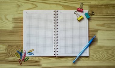Tahta masadaki okul malzemeleri: açık defter, kalem, iğne ve cilt klipsleri