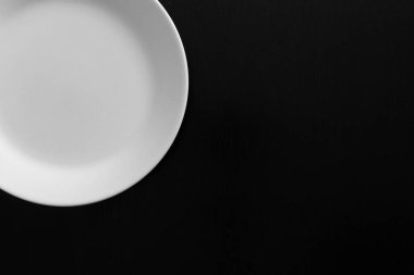 Siyah ahşap masada boş beyaz tabak. Mutfak aletleri kapatın.
