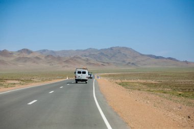 Moğolistan 'ın Ulgii kenti yakınlarında asfalt yolu olan bir manzara. Yoldaki ayırt edici Rus off-road aracı.