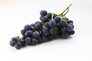 Siyah üzümler, beyaz arka planda yeşil yapraklı büyük taze meyveler