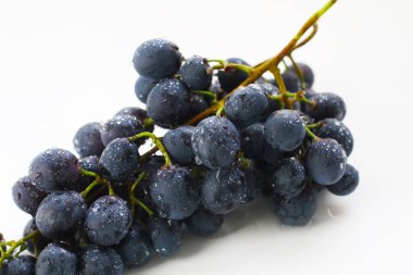 Siyah üzümler, beyaz arka planda yeşil yapraklı büyük taze meyveler