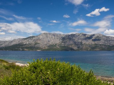 Hvar Adası, taze yeşil çimen, mavi gökyüzü ve dağlar ile Hırvatistan güzel kıyısında bir yol