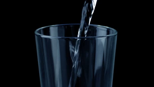 L'eau verse dans le verre sur le noir 