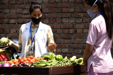 Dehradun, Uttarakhand / Hindistan - 15 Ağustos 2020: Sokak satıcılarından sebze satın alan sağlık görevlisi.