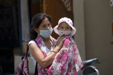 Dehradun, Uttarakhand / Hindistan - 15 Ağustos 2020: Kadınlar çocuğuyla yüz maskesi takıyor, sosyal mesafeyi koruyorlar.