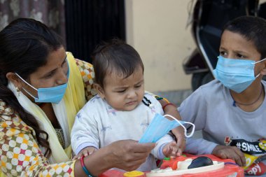 Dehradun, Uttarakhand / Hindistan - Eylül 06 2020: Hintli anne Corona virüsünden korunmak için bebek yüzüne maske takıyor.