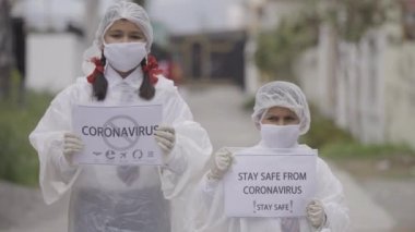 COVID-19 Coronavirüs - Ölümcül virüs: COVID-19 Coronavirus 'a karşı güvenlik için maske takan çocuklar, eldiven ve koruma elbisesi. Apple ProRes 422. Çocuklar farkındalık yaratıyor.