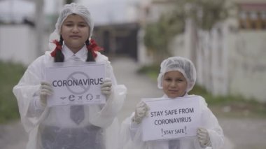 COVID-19 Coronavirüs - Ölümcül virüs: COVID-19 Coronavirus 'a karşı güvenlik için maske takan çocuklar, eldiven ve koruma elbisesi. Apple ProRes 422. Çocuklar farkındalık yaratıyor.
