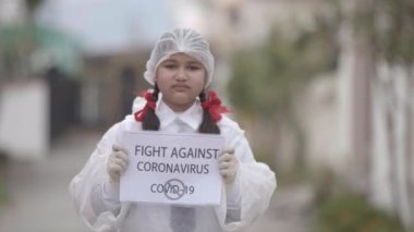 COVID-19 Coronavirüs - Ölümcül virüs: Maske takan kız, COVID-19 Coronavirus 'a karşı güvenlik için okul üniforması içinde eldiven ve koruma elbisesi. Apple ProRes 422. Kız farkındalık yaratıyor.