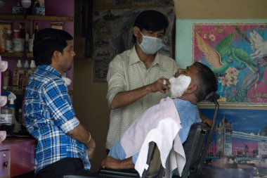 Dehradun, Uttarakhand / Hindistan - Eylül 2020: Salon sahibi maske takan bir adamı tıraş ediyor.
