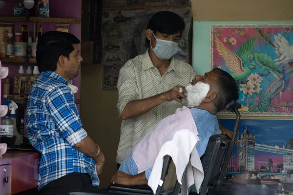Dehradun, Uttarakhand / Hindistan - Eylül 2020: Salon sahibi maske takan bir adamı tıraş ediyor.