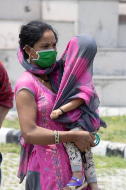 Dehradun, Uttarakhand / Hindistan - Eylül 08 2020: Çocuğuyla birlikte maskeler takan bir anne çocuğunu bir bezle örter.
