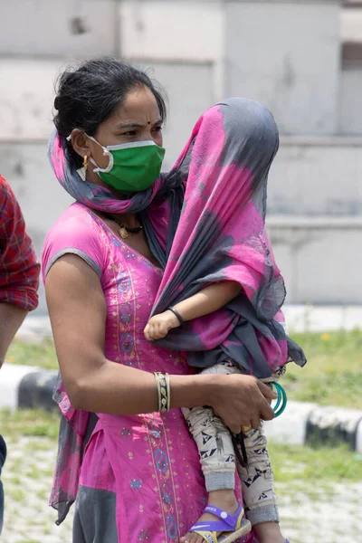 Dehradun, Uttarakhand / Hindistan - Eylül 08 2020: Çocuğuyla birlikte maskeler takan bir anne çocuğunu bir bezle örter.