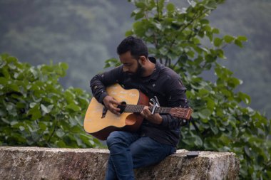 Güzel tepelerde gitar çalan bir genç..