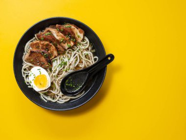 Sarı arka planda Ramen Erişte ve Tavuk Çorbası. Izgara tavuk, erişte ve siyah bir kasede yumurta. Üst Manzara. Kapat..