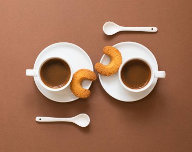 Kahverengi arka planda fotokopi alanı olan beyaz kahve fincanları. Kurabiyeli küçük bardaklarda siyah espresso. Kahve konsepti. Üst görünüm.