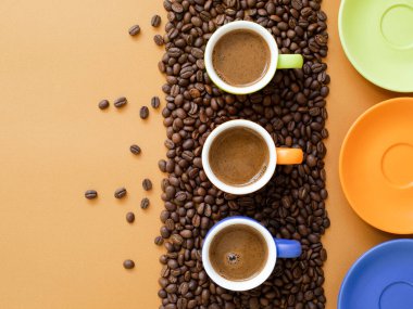 Kahverengi arkaplanda kahve çekirdekleri ve fotokopi alanı olan renkli kahve fincanları. Küçük bardaklarda siyah espresso. Kahve konsepti. Üst görünüm.